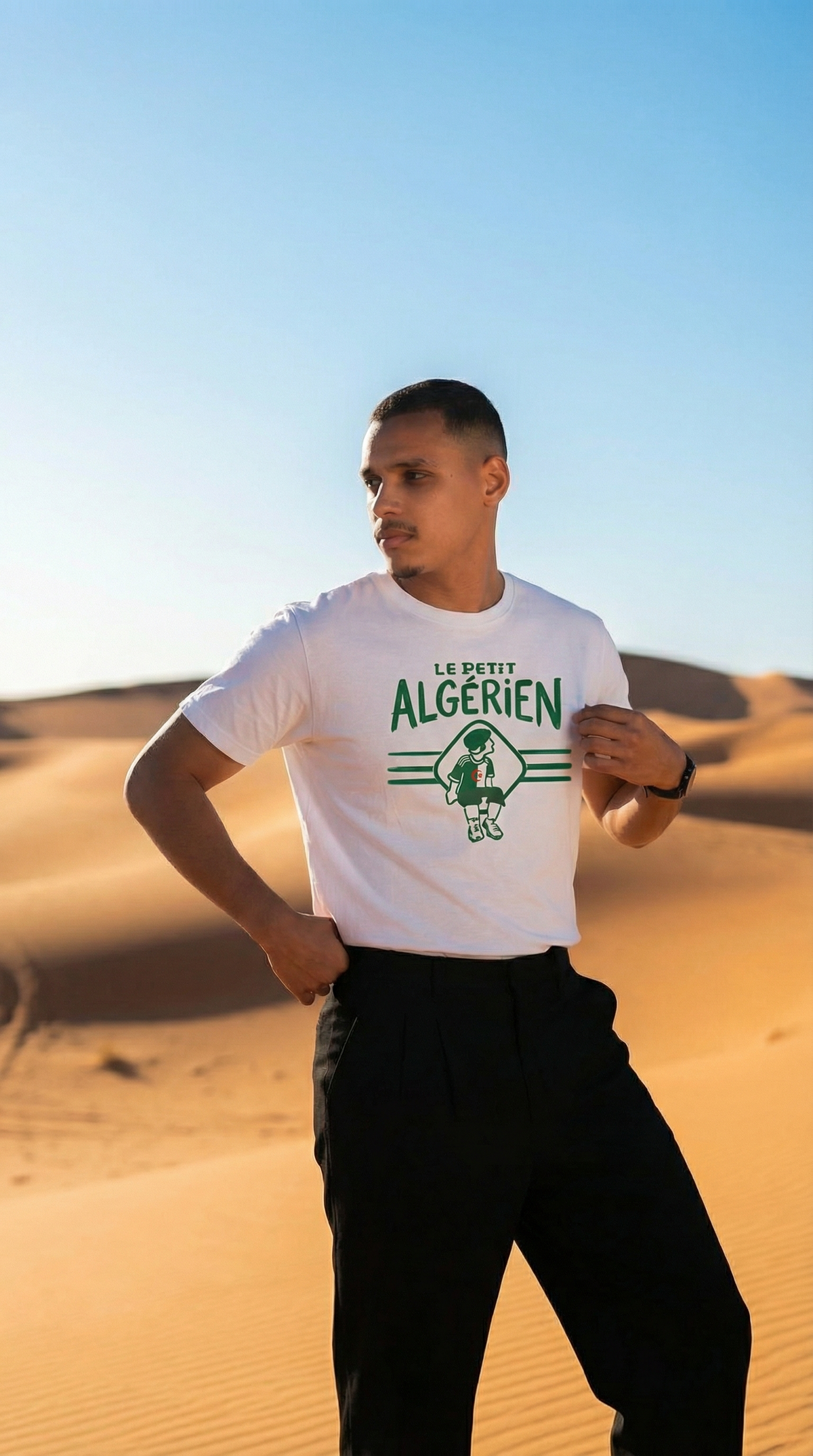 T-shirt blanc Le Petit Algérien, motif vert au centre, porté par un homme tenant le tissu sur le côté.